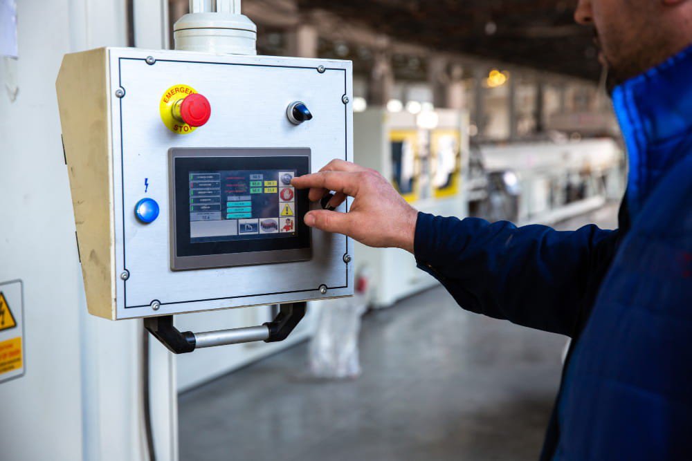 Operaio utilizza il pannello touch di un PLC per controllare un macchinario in linea di produzione