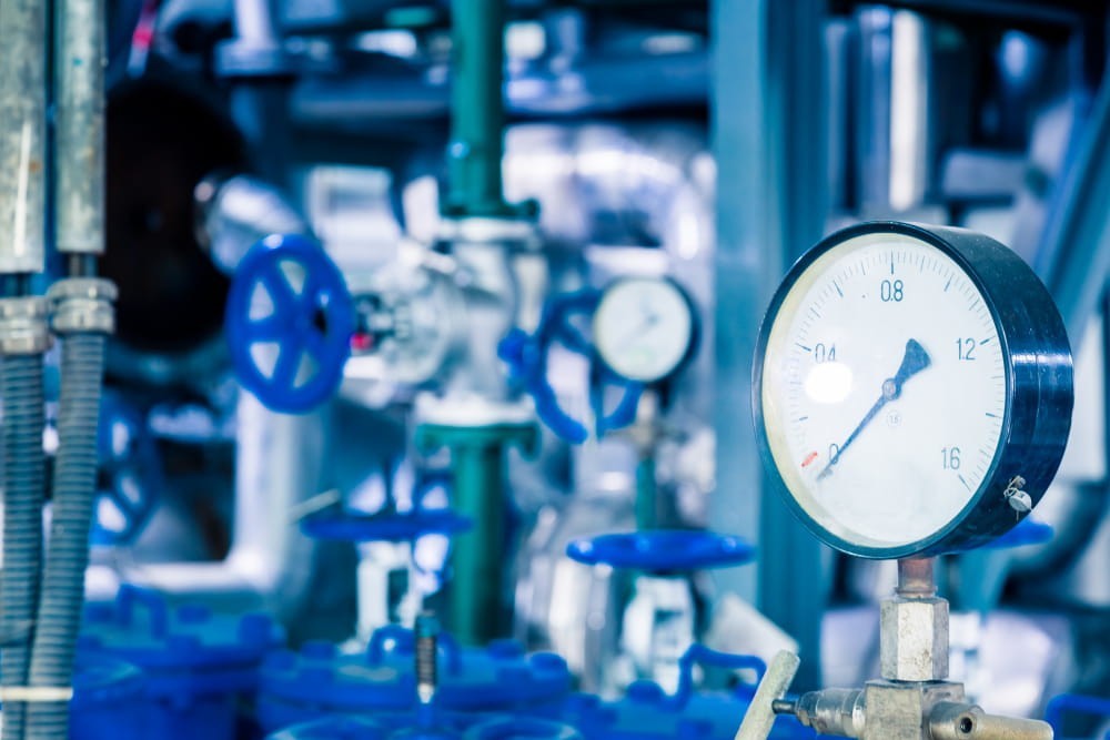 Manometro e valvole blu su un impianto di raffreddamento industriale, strumenti che il tecnico controlla per il monitoraggio del chiller.