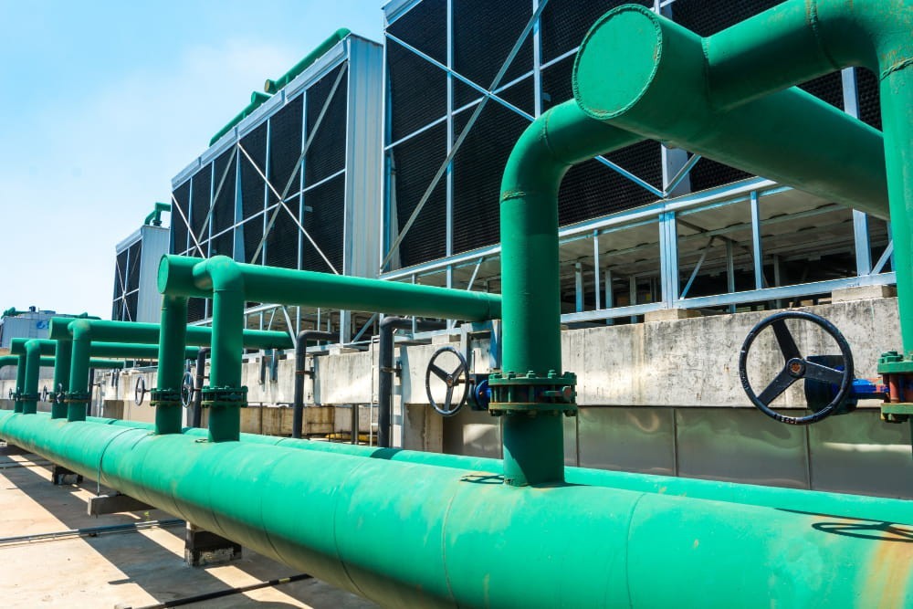 Torri di raffreddamento industriali con tubazioni verdi su un tetto, parte di un impianto di refrigerazione che un operatore tecnico deve saper gestire.